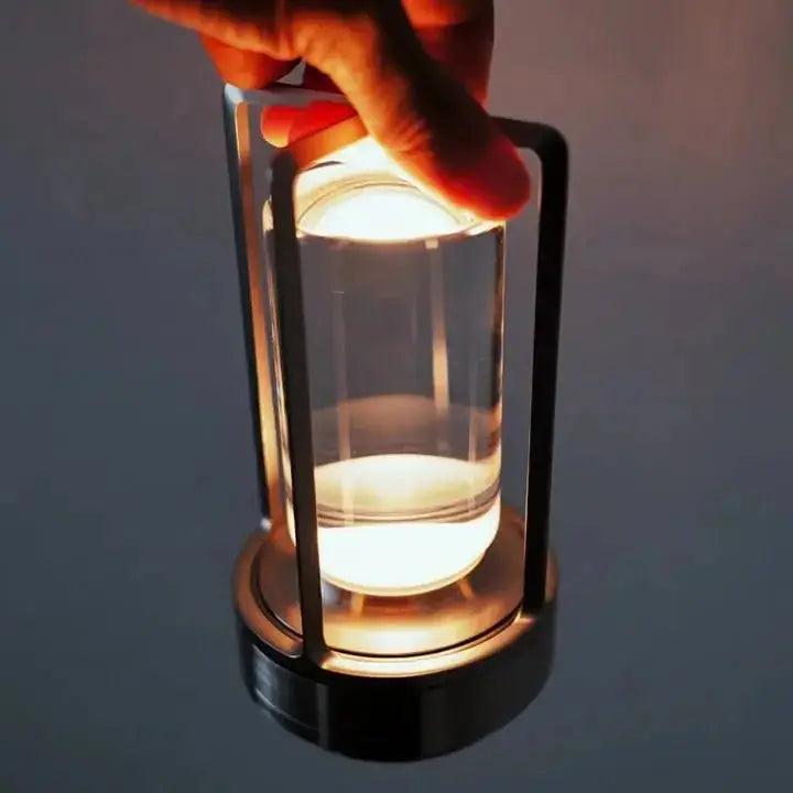 Hand holding Zenvia Essentials' Elegant Crystal Rechargeable Table Lamp, a small glass lantern with black metal base.