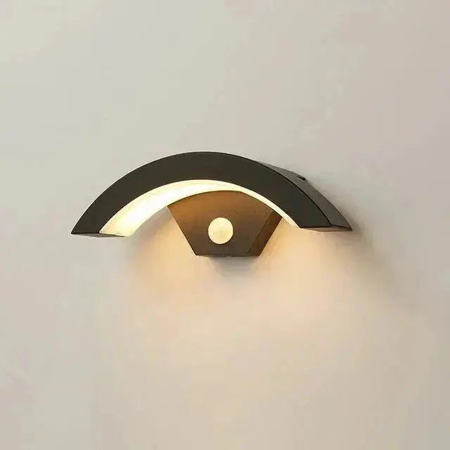 Black metal Zenvia Essentials Modern Curved LED Motion Sensor Wall Light with white bulb on a white wall.